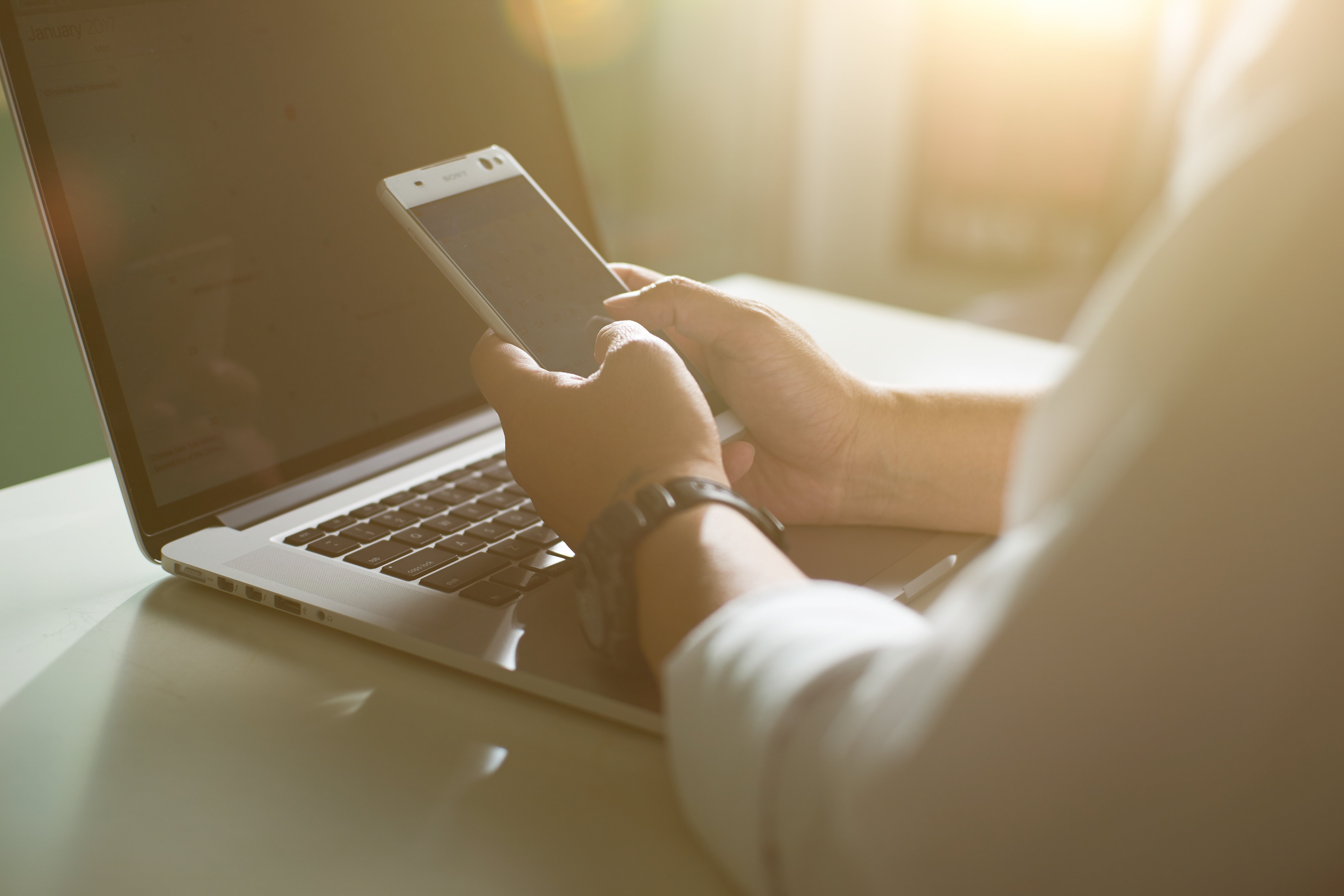 graphicstock-silhouette-of-cropped-shot-of-a-young-man-working-from-home-using-smart-phone-and-notebook-computer-mans-hands-using-smart-phone-in-interior-man-at-his-workplace-using-technology-flare-light_r_exHw3vejg